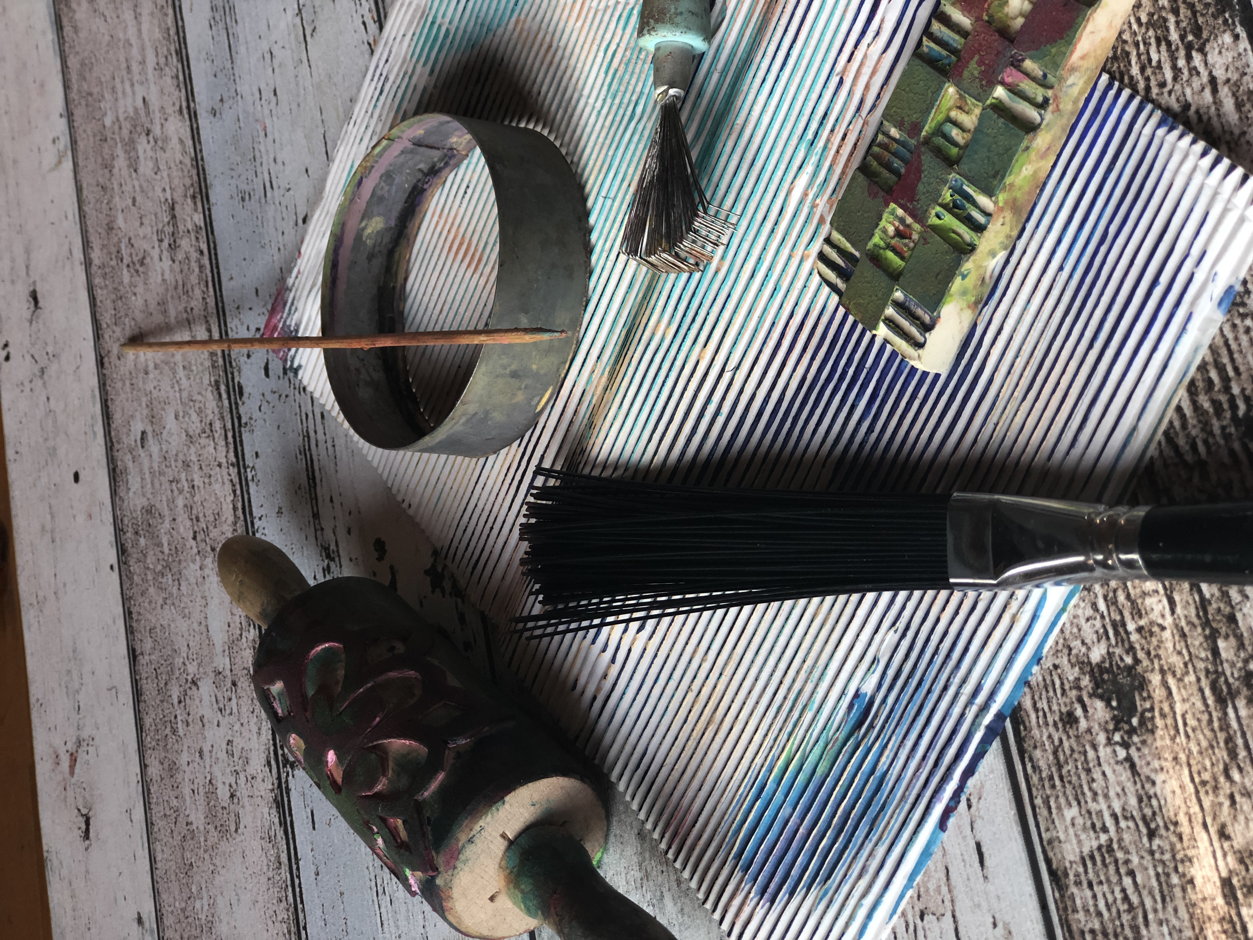 A patterned roller, comb, metal tools and paint-marked cardboard on a studio table